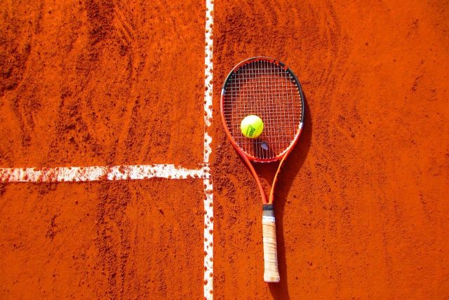 Una pista de tenis de tierra batida, las mismas del torneo de tenis Roland Garros, con una raqueta y una pelota de tenis.
